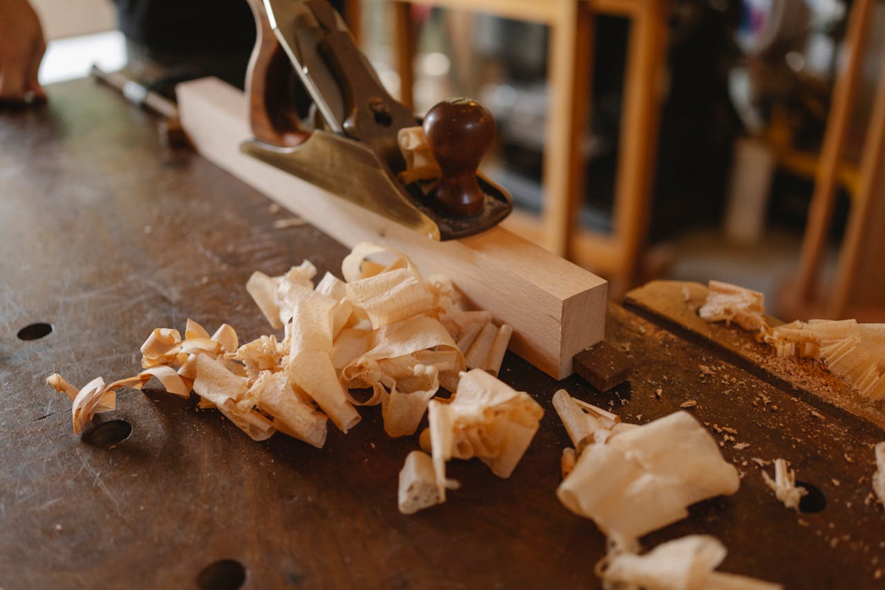 Close-up of a woodworking process with hand plane and wood shavings on a workbench.